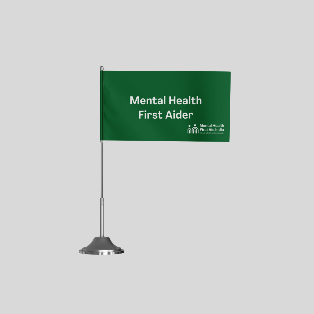 A green tabletop sign with white text reading 'Mental Health First Aider' on a silver stand, shown against a light gray background.