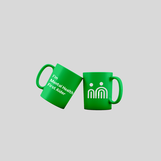 Two bright green ceramic mugs on a light gray background. One mug is tilted and reads 'I'm Mental Health First Aider' in white text, and the other shows a white 'm' symbol with small dot eyes.