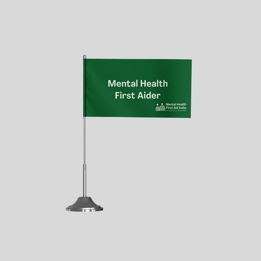 A green tabletop sign with white text reading 'Mental Health First Aider' on a silver stand, shown against a light gray background.